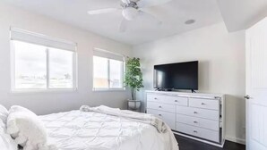 Un dormitorio con cama, cómoda, televisor y ventilador de techo.