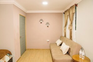 A room with a beige sofa, two wall-mounted light fixtures, a door, and a window with curtains.