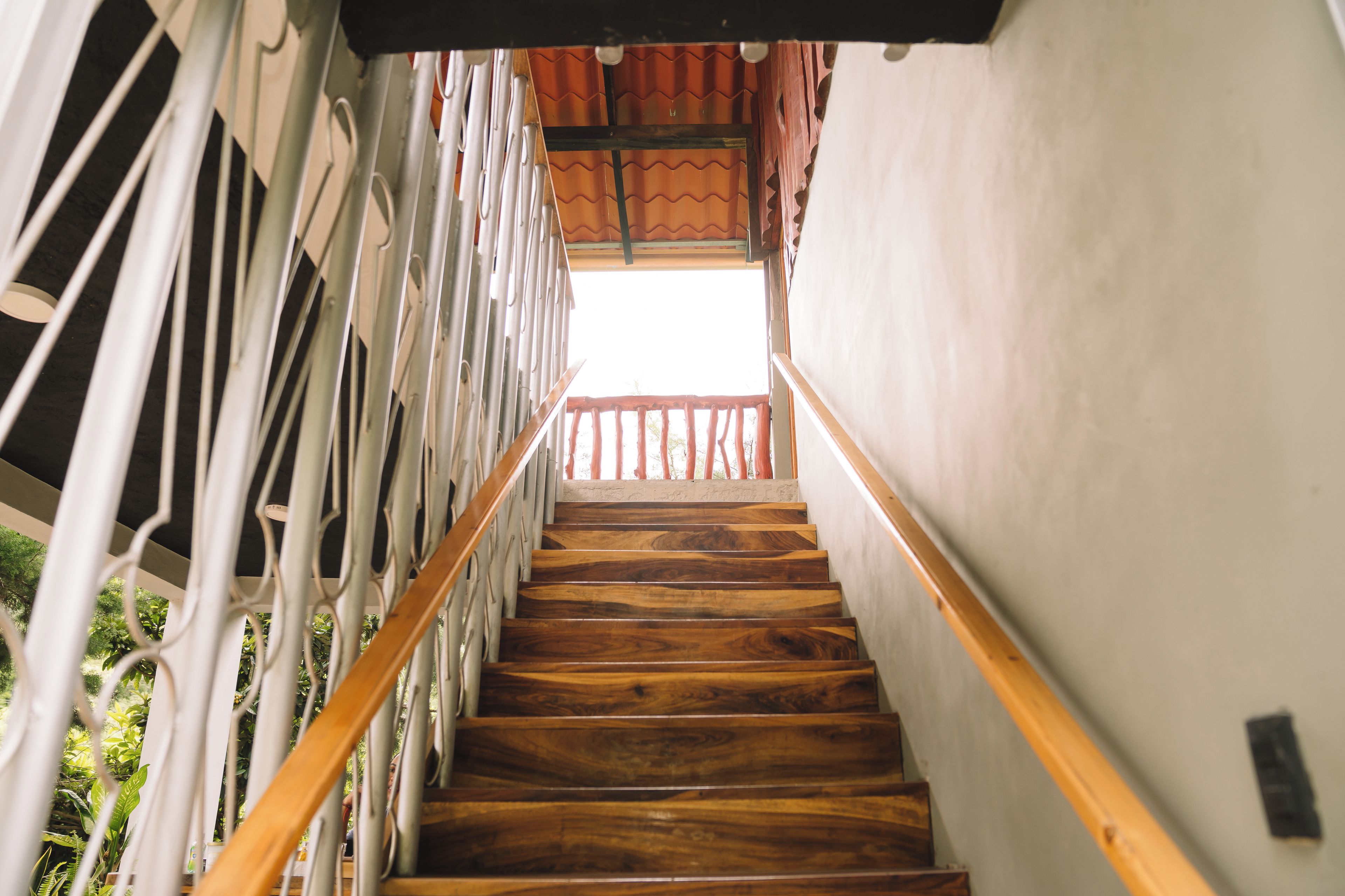 Un escalier en bois avec une rampe en métal, menant à un balcon d’où l’on peut admirer la verdure.