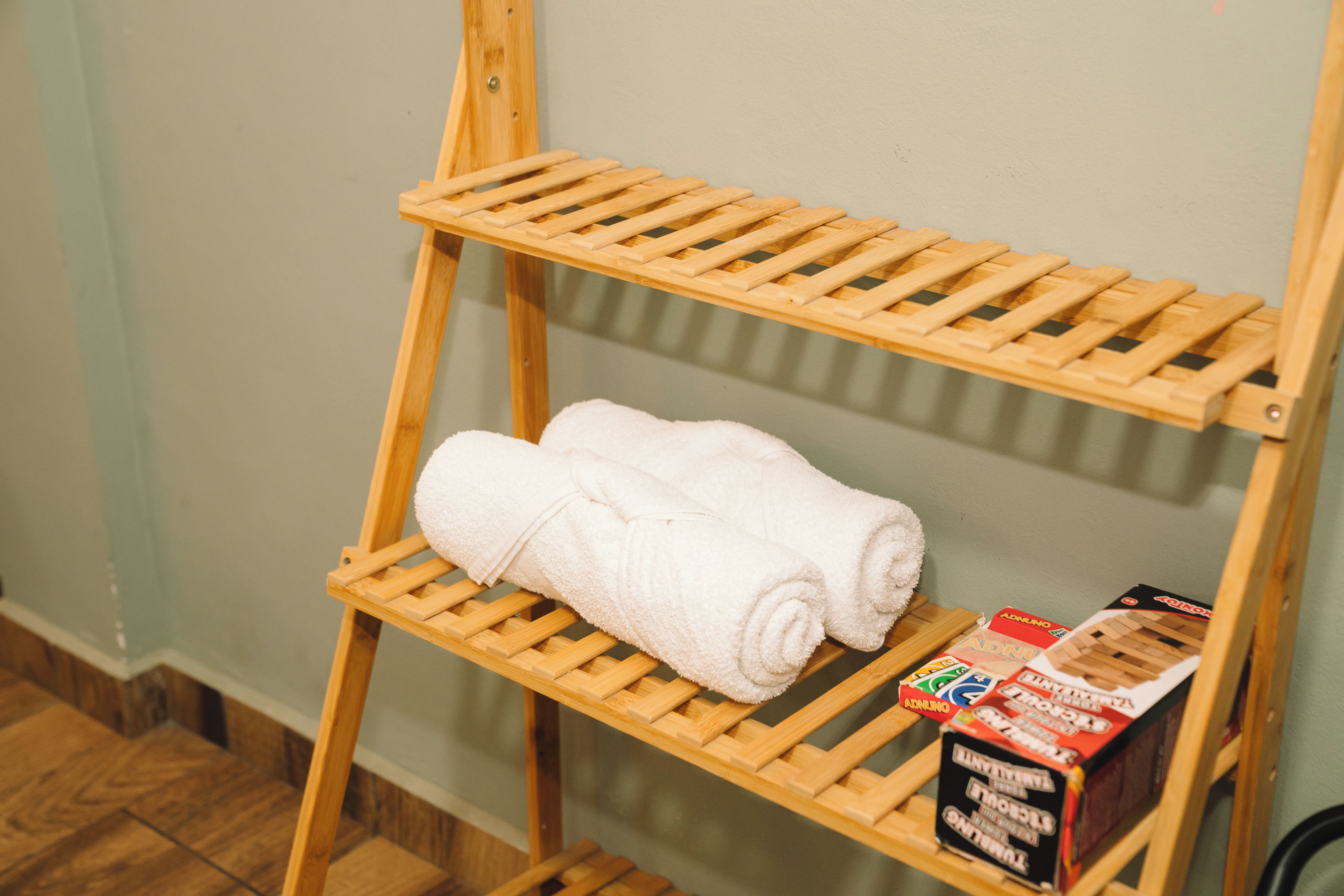 A wooden shelf with two rolled white towels and a box of Adnino body wash.