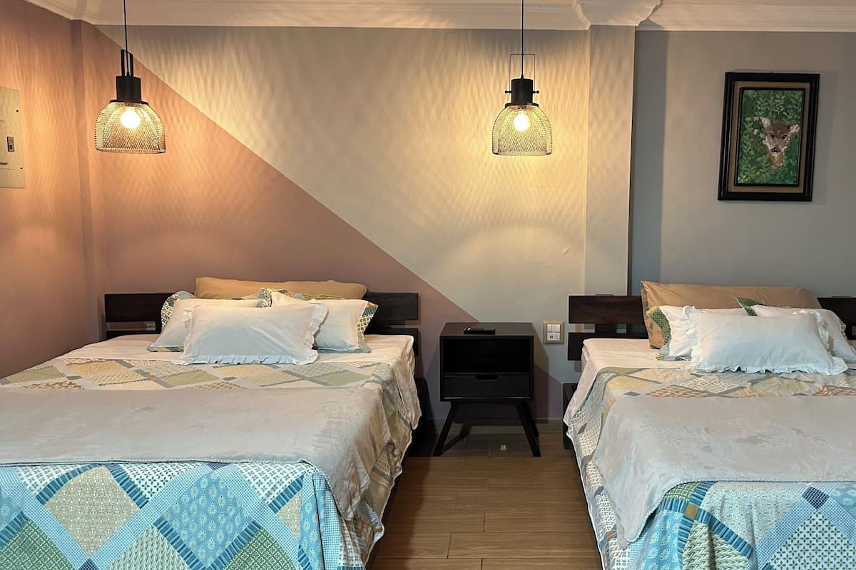 Een hotelkamer met twee bedden, elk met beddengoed met een patroon, een nachtkastje, een aan de muur hangend schilderij en twee hangende lampen.