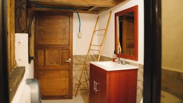 A bathroom with a wooden door, a white sink, a mirror, and a wooden ladder leaning against the wall.