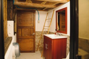 Een badkamer met een houten deur, een wit wastafelmeubel, een spiegel en een houten ladder tegen de muur.