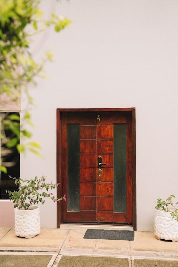 A wooden door with a number '4' above it, flanked by two white planters with green plants.