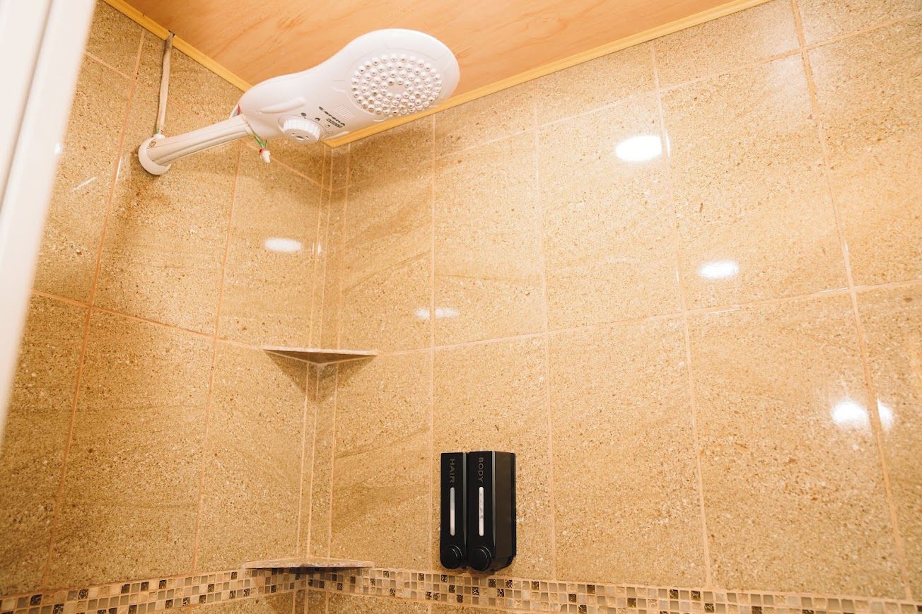 Zona de ducha con cabezal de ducha de mano y panel de control en la pared.