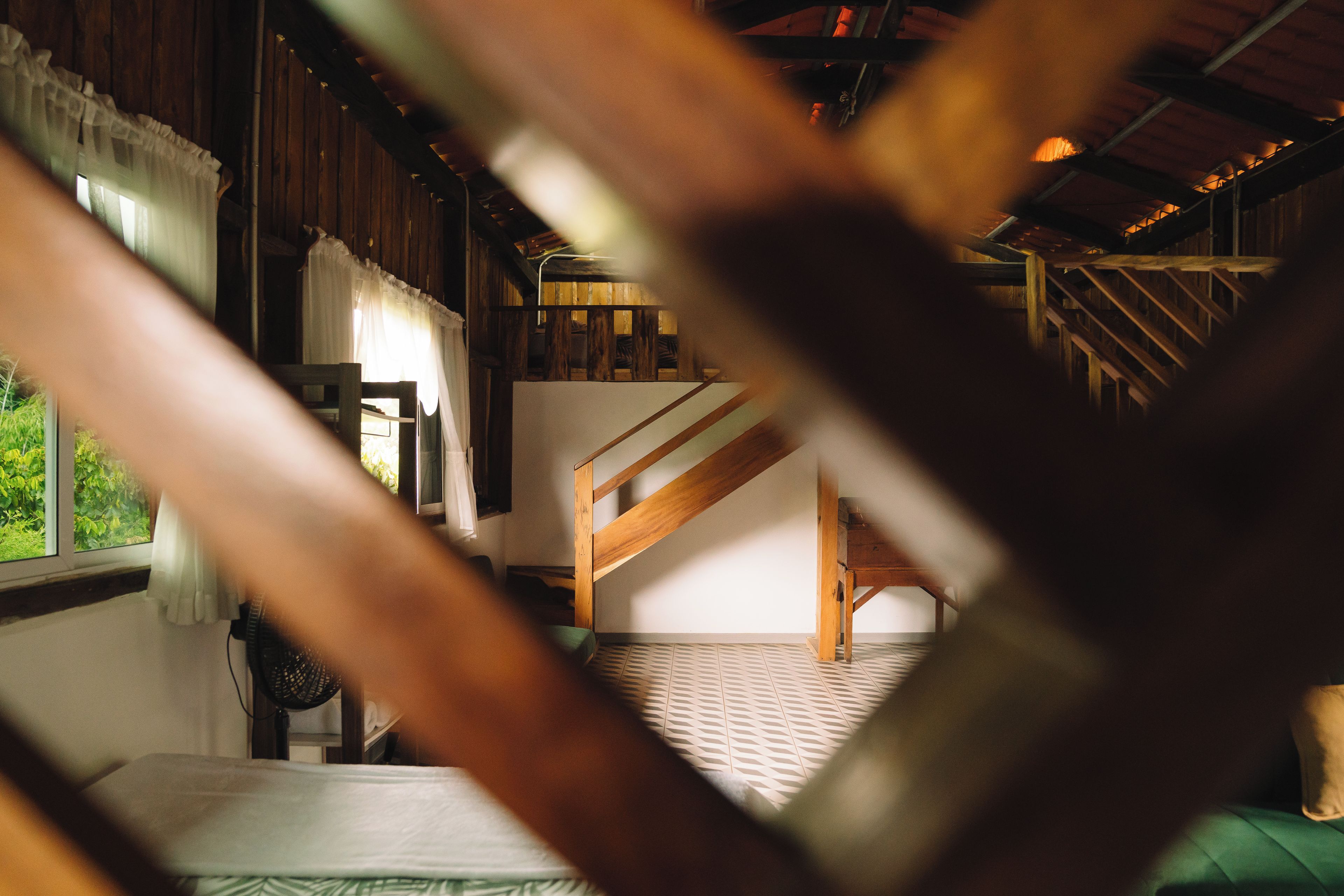 Quarto com escada de madeira, cama e janela com cortinas.