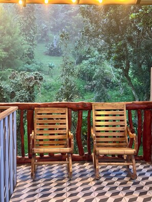 Dos sillas de madera con respaldos de listones en un balcón con suelo a cuadros, con vistas a un paisaje verde y exuberante.