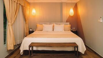 Un dormitorio con una cama de madera, dos mesitas de noche, un banco y una ventana con cortinas.