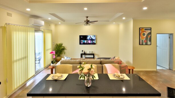 A modern living room with a black dining table, beige sofa, and a ceiling fan. - F2 - Pool, Inverter, Gym, Pavilion, Wifi, Perfect for Kids - Ibex Meanwood! (Lusaka)