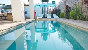 A swimming pool with lounge chairs and a blue umbrella. - F2 - Pool, Inverter, Gym, Pavilion, Wifi, Perfect for Kids - Ibex Meanwood! (Lusaka)