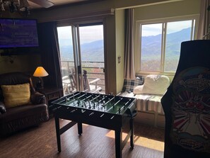 A cozy room with a foosball table, a comfortable sofa, a TV, and a window with a mountain view.