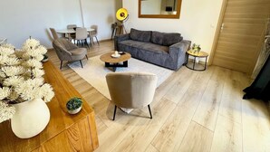 A modern living room with a grey sofa, two armchairs, a coffee table, a dining table with chairs, a mirror, and a wooden door. - Superb 3 P with balcony view near beach (Antibes)