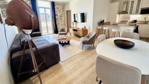 A modern living room with a sofa, coffee table, and dining area. There is a kitchen with white cabinets and a flat-screen TV mounted on the wall. - Superb 3 P with balcony view near beach (Antibes)