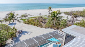 A beach view with a pool area, including a covered seating area with umbrellas and lounge chairs. - Book your stay now and experience the magic of Waters Edge! (Sanibel)