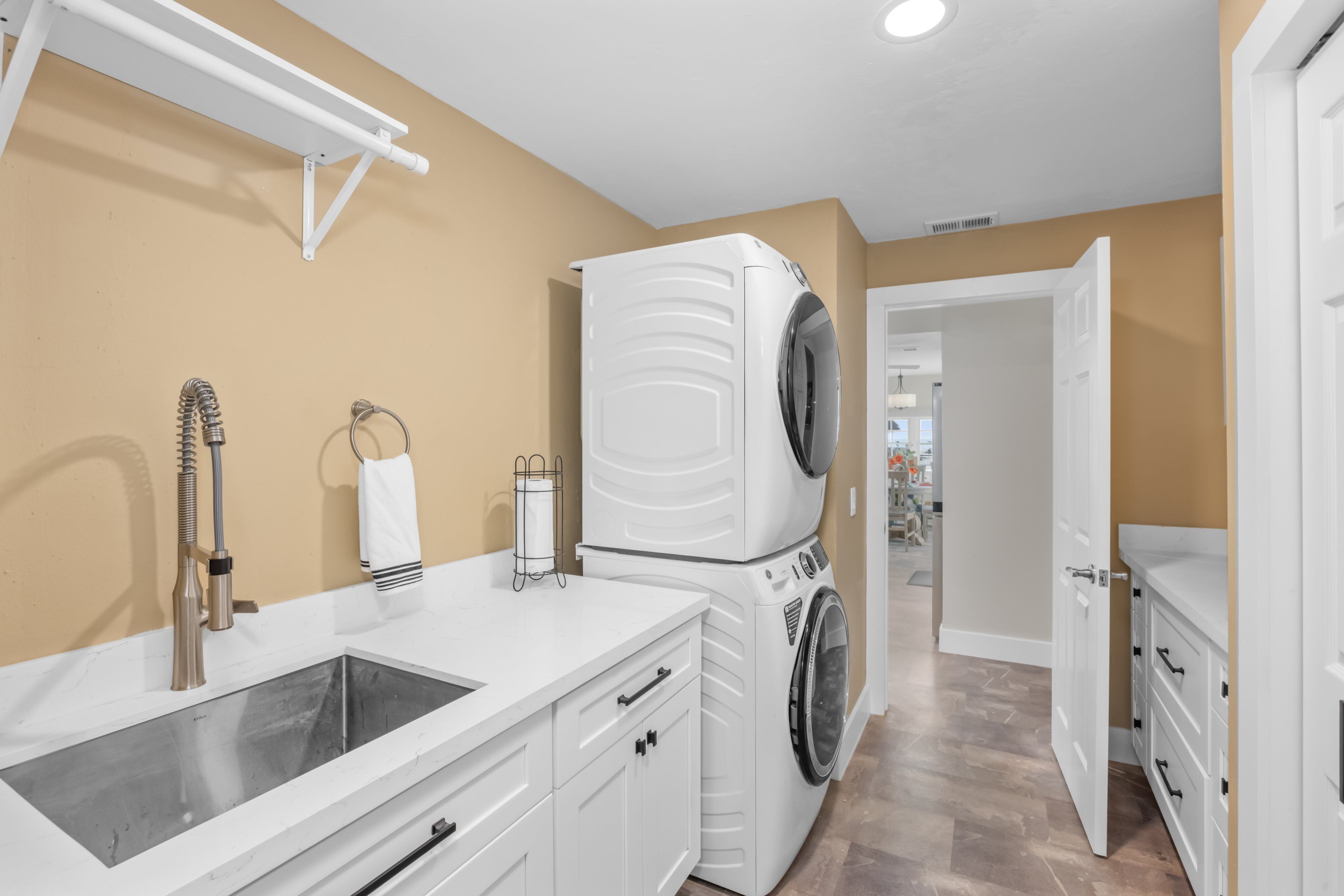 A laundry room with stacked washers and dryers, a sink, and a towel rack.