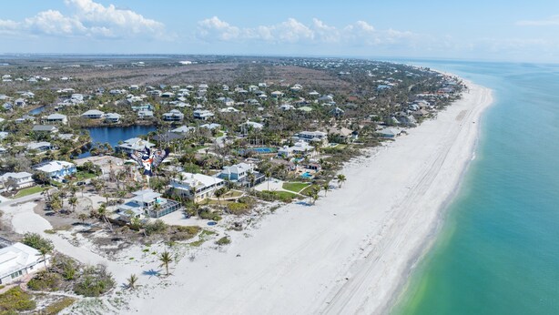 An aerial view of a coastal residential area with houses, a beach, and a clear blue sky. - Book your stay now and experience the magic of Waters Edge! (Sanibel)