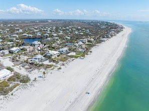 An aerial view of a coastal residential area with houses, a beach, and a clear blue sky.