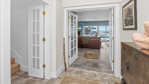 A hallway with a staircase, a wooden door with glass panels, a brown leather sofa, and a view of the ocean through large windows. - Book your stay now and experience the magic of Waters Edge! (Sanibel)