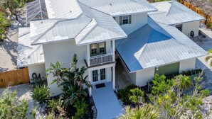 A two-story house with a metal roof, surrounded by a sandy beach and palm trees. - Book your stay now and experience the magic of Waters Edge! (Sanibel)