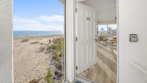A beach view from a room with a white door labeled 202, wooden flooring, and a small seating area with a table and chairs. - Your Front Yard? The Gulf of Mexico – Blue Gulf 202 Beachfront Condo (Sanibel)