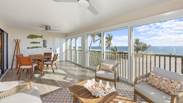 A spacious balcony with a view of the ocean, wooden furniture, and a ceiling fan. - Your Front Yard? The Gulf of Mexico – Blue Gulf 202 Beachfront Condo (Sanibel)