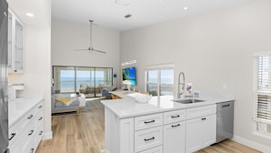 A modern kitchen with white cabinetry, a large island, and a view to the outside. - Your Front Yard? The Gulf of Mexico – Blue Gulf 202 Beachfront Condo (Sanibel)