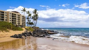 A beachfront hotel with multiple floors, palm trees, and a rocky shoreline. - 3 bedrooms 3 baths • Oceans views • Steps to beach (Kihei)