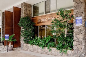 A hotel entrance with a stone facade, a wooden sign reading "PACIFIC MONARC," and a guest parking sign. - Ocean View•1 BR Corner Condo•Mins to Waikiki Beach (Honolulu)