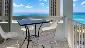 A balcony with a table and chairs, overlooking a clear blue sea and a distant shoreline.