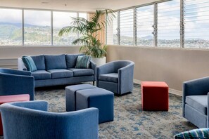 A modern lounge area with a sofa, armchairs, and ottomans, featuring a city view through large windows. - Ocean View•1 BR Corner Condo•Mins to Waikiki Beach (Honolulu)