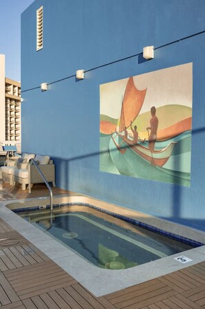 Un espace piscine agrémenté d’une fresque représentant une personne qui rame dans un bateau, de chaises longues et d’une terrasse en bois.
