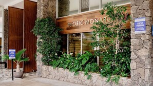 A hotel entrance with a stone facade, a wooden sign reading "PACIFIC MONARC," and a guest parking sign.