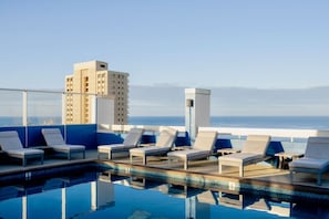 Un espace piscine aménagé sur le toit, avec des chaises longues et une vue dégagée sur l’océan.