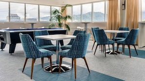 A modern lounge area with a pool table, comfortable seating, and large windows offering a city view.