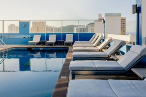 Une piscine sur le toit, dotée de chaises longues et offrant une vue sur les bâtiments.
