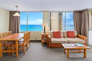 A hotel room with a dining table, chairs, a sofa, a lamp, and a view of the ocean. - Ocean View•1 BR Corner Condo•Mins to Waikiki Beach (Honolulu)