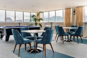 Un espace de détente moderne doté d’une table de billard, de sièges confortables et de grandes fenêtres offrant une vue sur la ville.