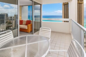 A balcony with a glass door, a sofa with red cushions, a round table, and white chairs. - Ocean View•1 BR Corner Condo•Mins to Waikiki Beach (Honolulu)