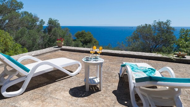 Um terraço com duas cadeiras de descanso brancas, uma mesinha com uma bebida e vista para o mar.