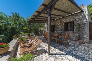 Un bâtiment en pierre doté d’un patio couvert, de sièges en plein air et de plantes en pot.