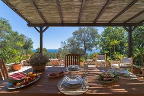 Un espace de restauration en plein air avec une table en bois disposée pour deux personnes, entourée de plantes en pot et offrant une vue panoramique.