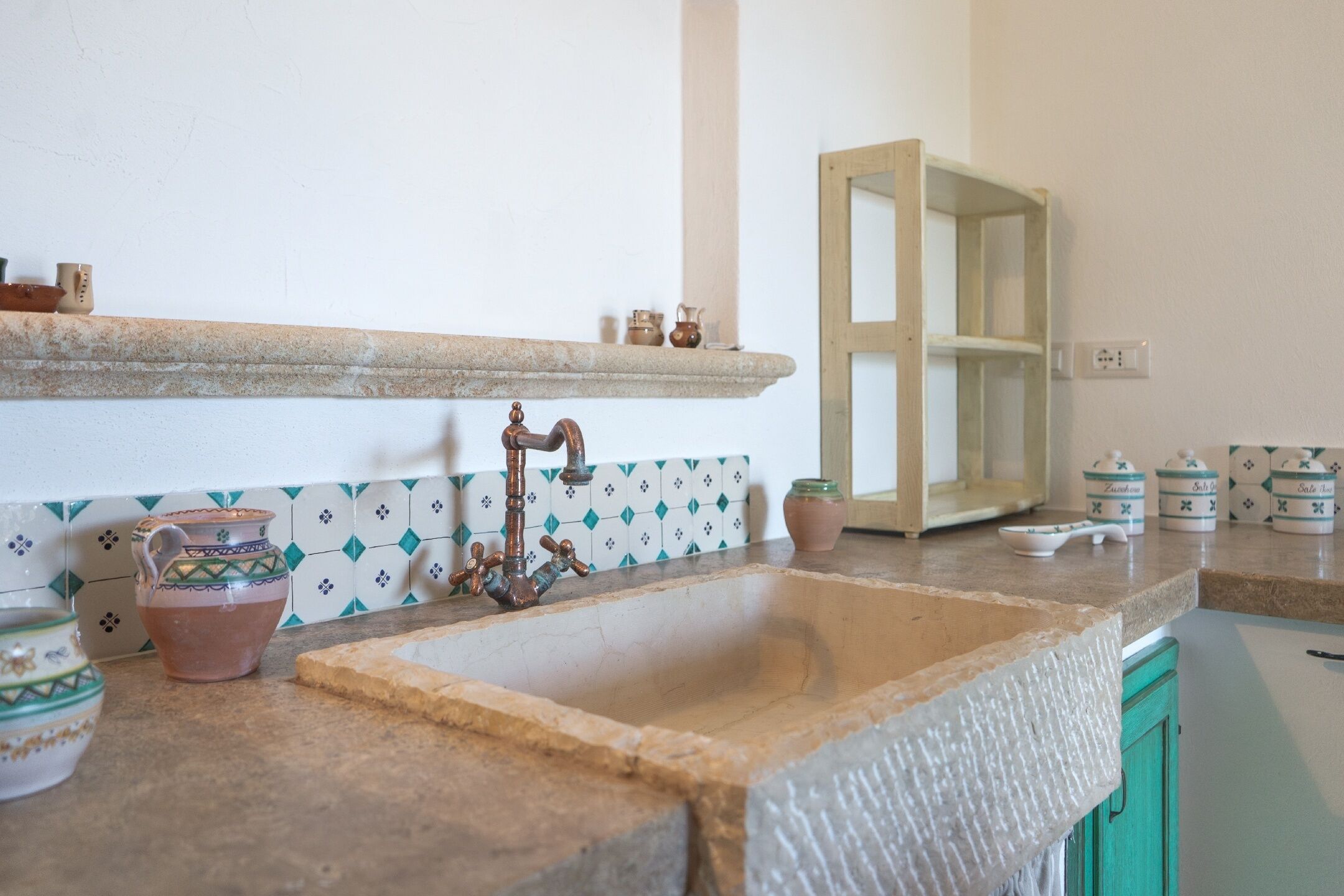 Une cuisine dotée d’un évier en pierre, de carreaux décoratifs et d’une étagère en bois où sont disposés de petits objets.