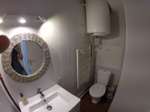 Bathroom features a sink, mirror, and toilet, with a radiator above the toilet and a tiled floor.