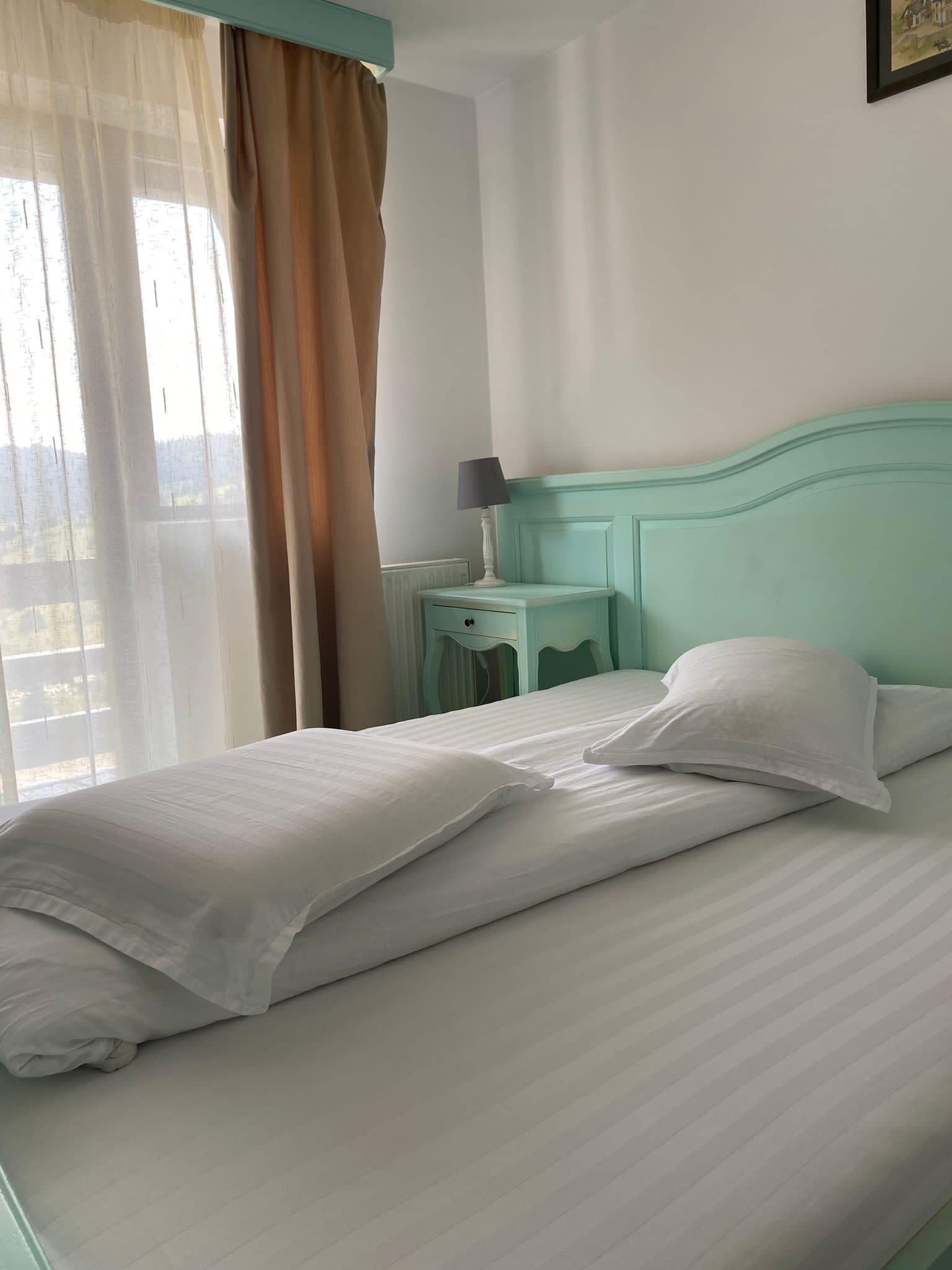 A neatly made bed with white linens in a room with a teal headboard.