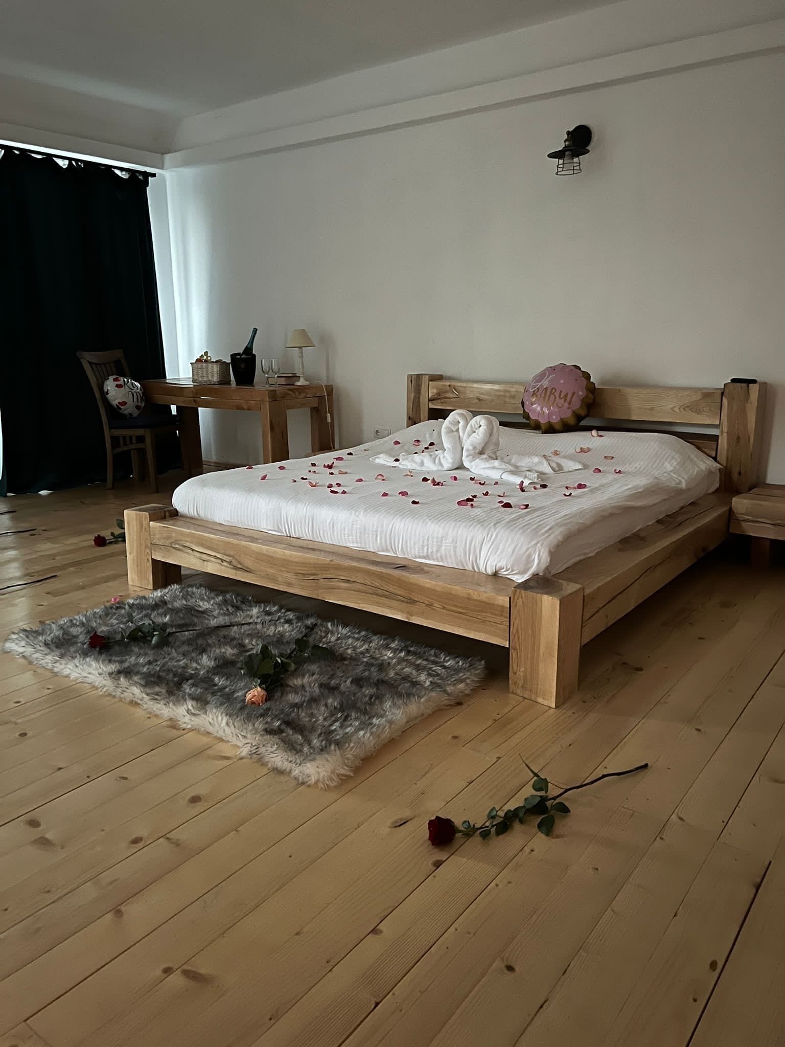 Una cama de madera con colcha blanca, un tapete mullido y una sola rosa en el suelo.