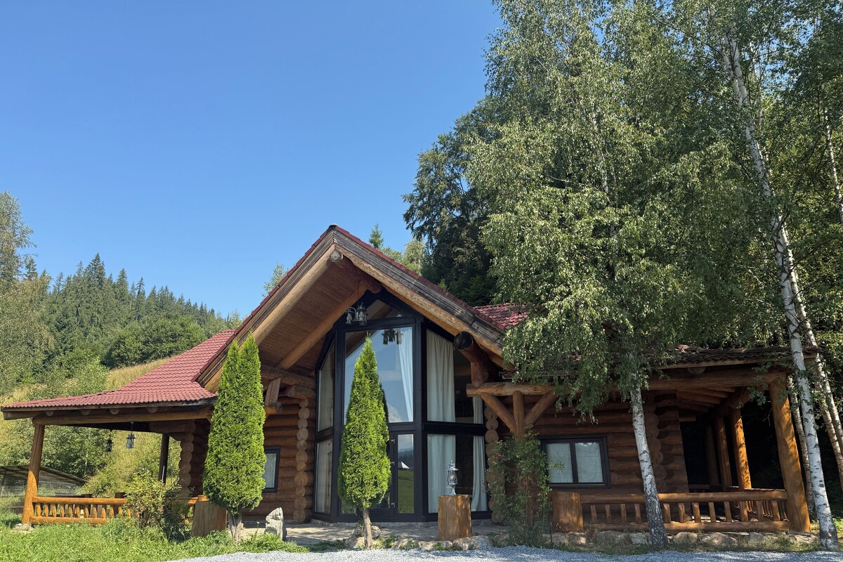 Eine Blockhütte mit rotem Ziegeldach, großen Fenstern und einer Veranda.