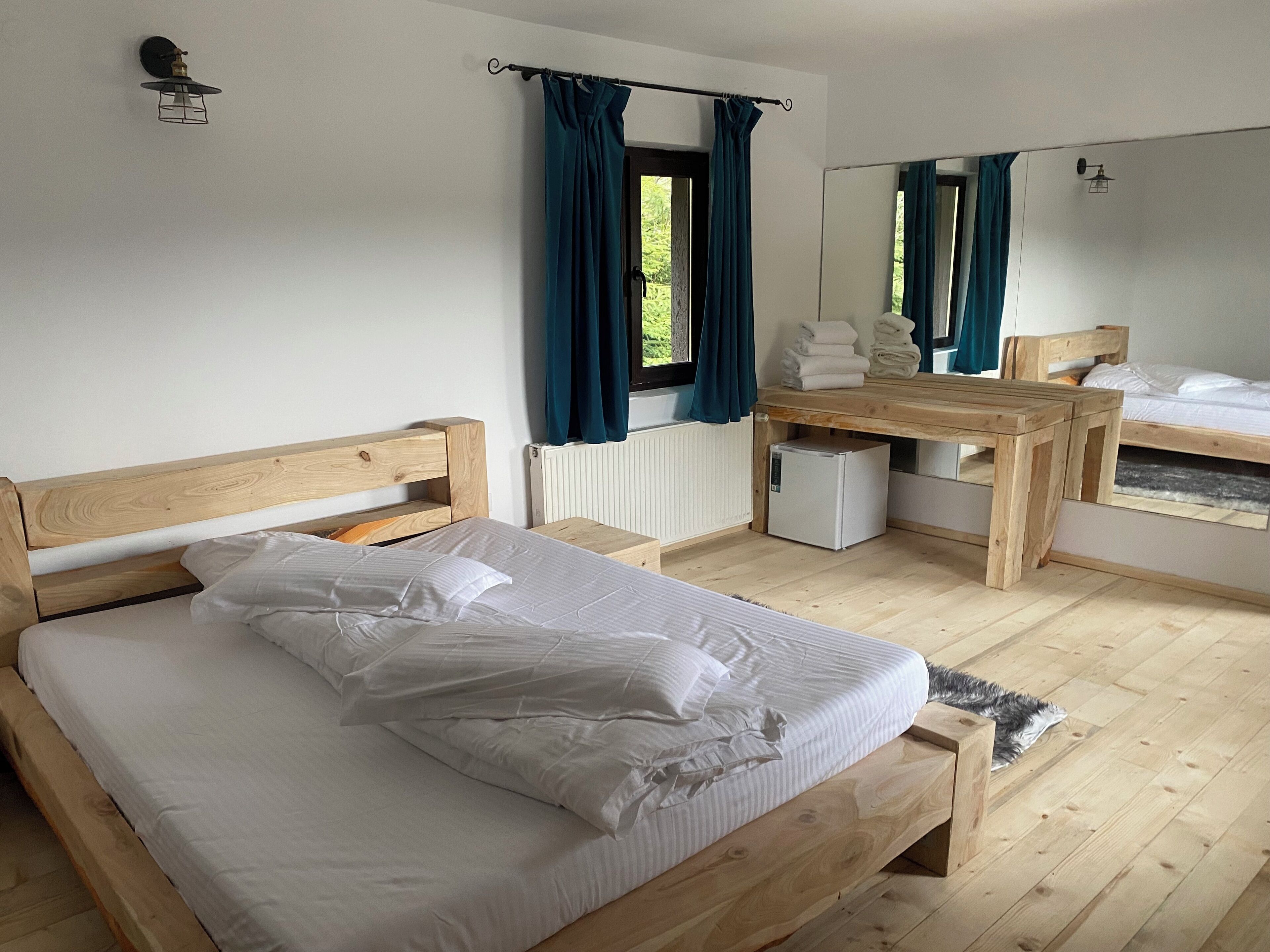 A bedroom with a wooden bed, a small wooden desk, a mirror, and a window with curtains.