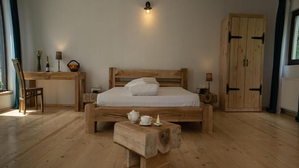 Un dormitorio con una cama de madera, mesitas de noche, un taburete pequeño de madera y un armario de madera.