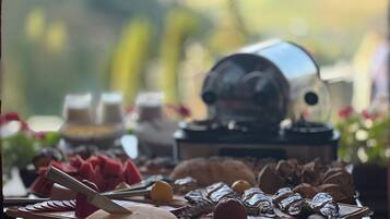 Una tabla de quesos con diferentes tipos de queso y acompañamientos, una cafetera y una vista panorámica al aire libre.
