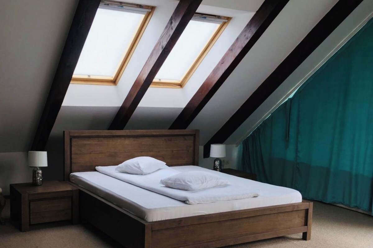 Ein Schlafzimmer mit einem hölzernen Bett, zwei Nachttischen, einem Oberlicht und Blick auf den Himmel.